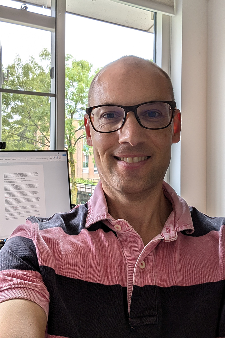 Michiel selfie met op de achtergrond computerscherm en uitzicht naar regenachtige omgeving